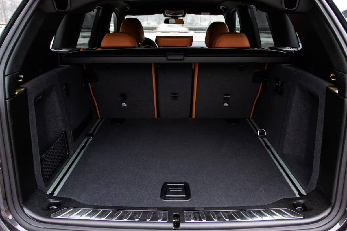 Interior view of a luxury SUV trunk, featuring dark carpeted flooring and orange leather accents on the rear seats.
