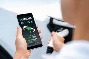 A person checks an electric vehicle charging app on their smartphone, displaying a 60% charge and 6 hours 10 minutes remaining.