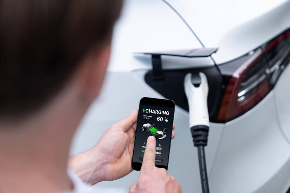 A person charging a white electric car using a smartphone app showing 60% battery status and charging progress.