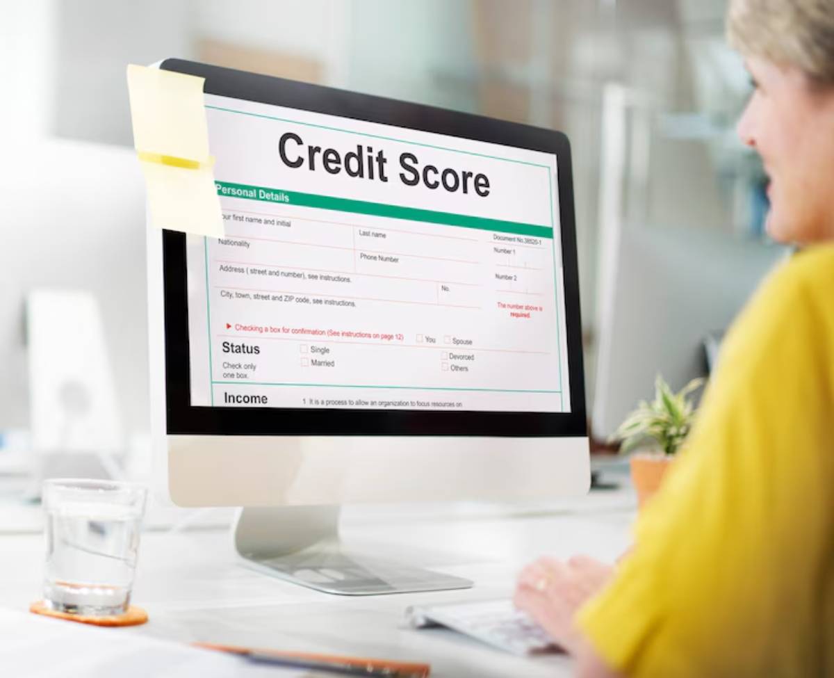 A person sitting at a desk fills out a digital credit score form on a computer screen, with a glass of water nearby.