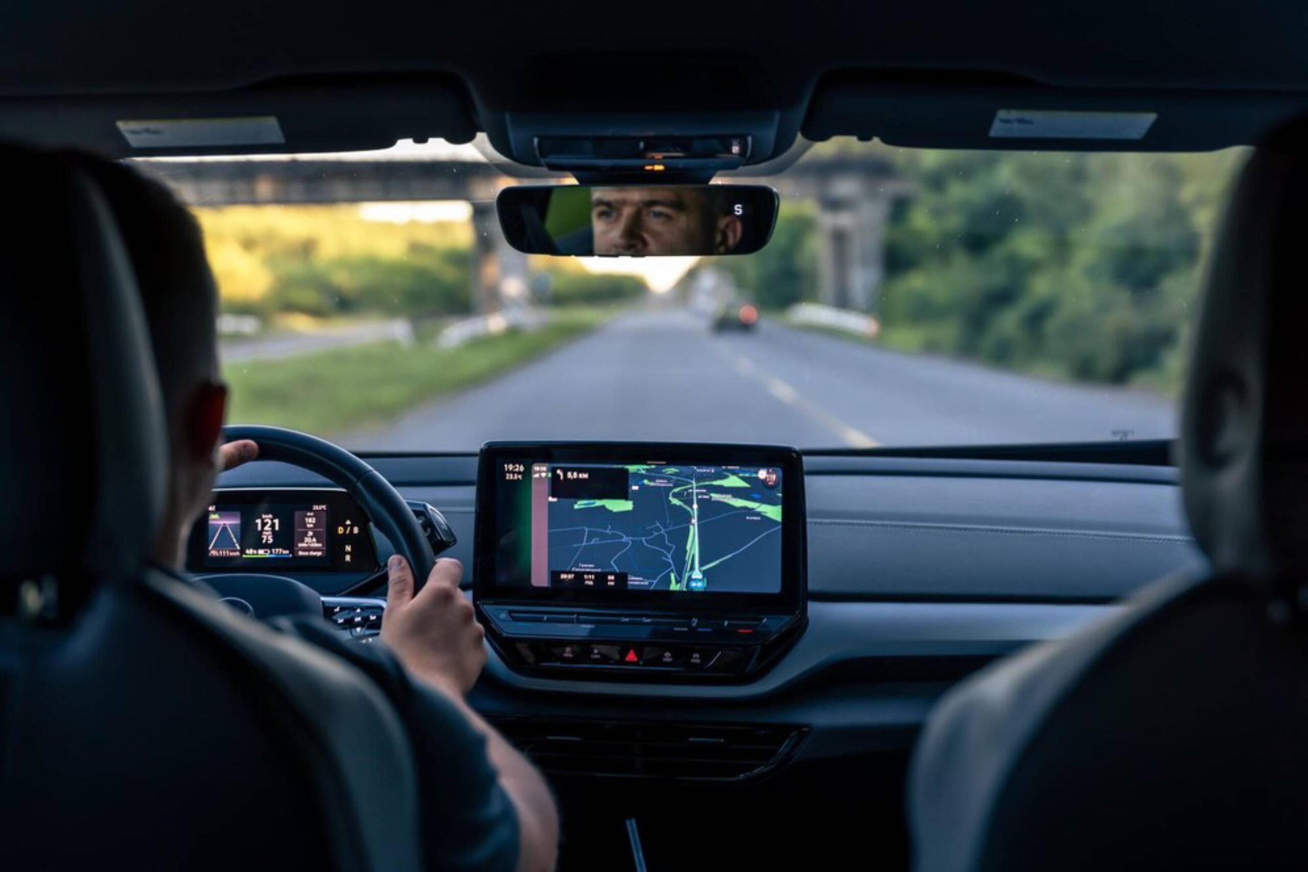 Inside a modern car, a driver grips the steering wheel while navigating a digital map displayed on the dashboard.