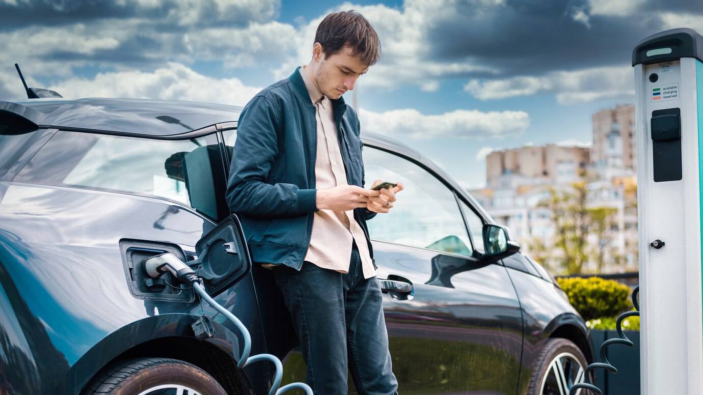 A person stands next to a black electric car.