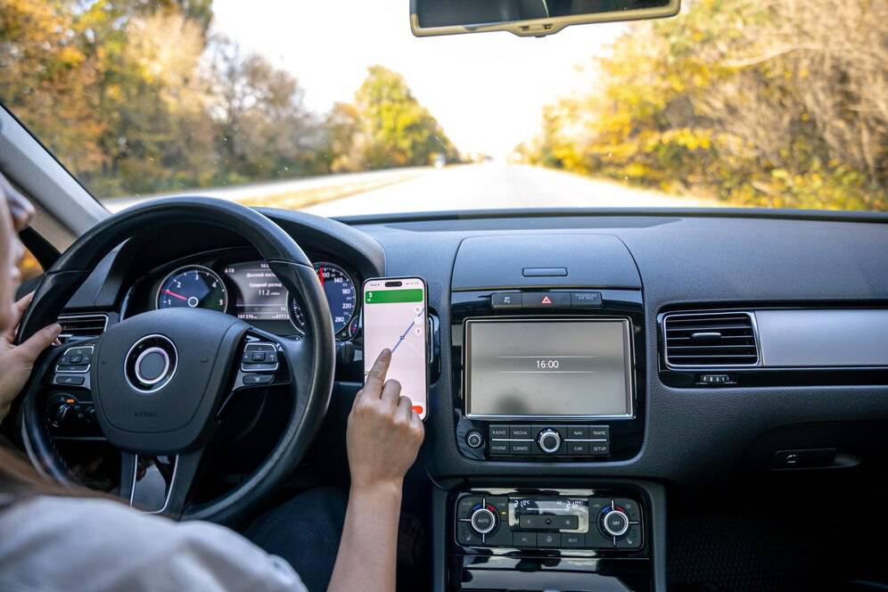 A driver holds a smartphone with navigation while steering a car on a deserted road, showcasing modern driving technology.