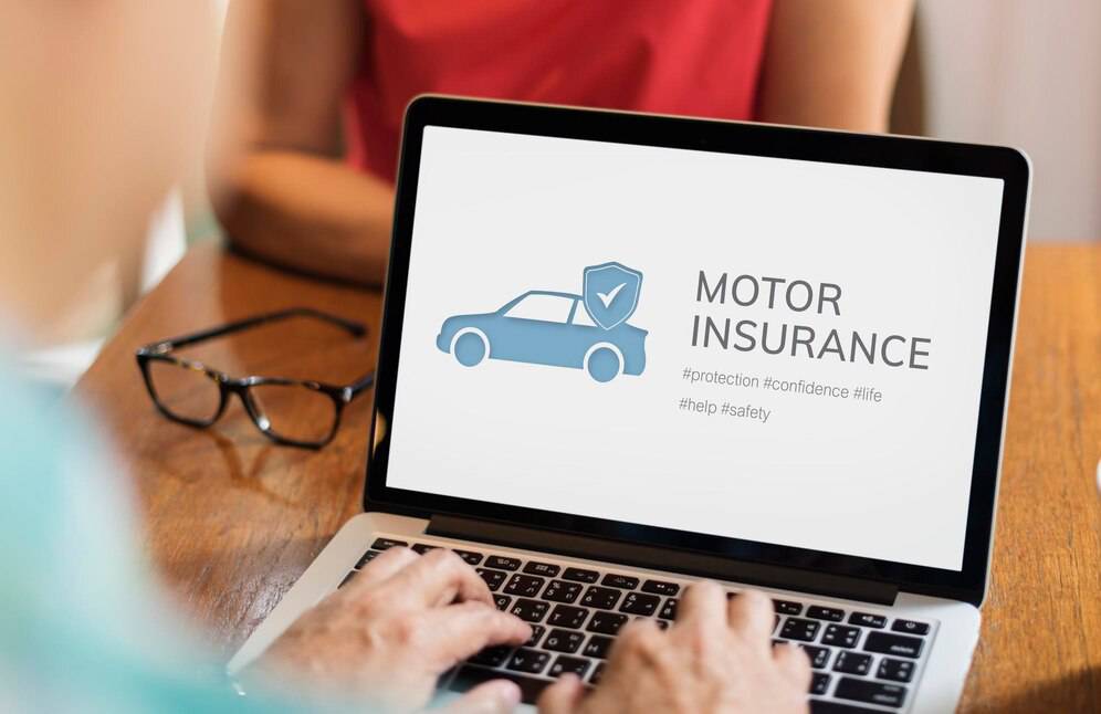 A person using a laptop at a wooden table, displaying a Motor Insurance graphic with keywords like #protection and #safety.