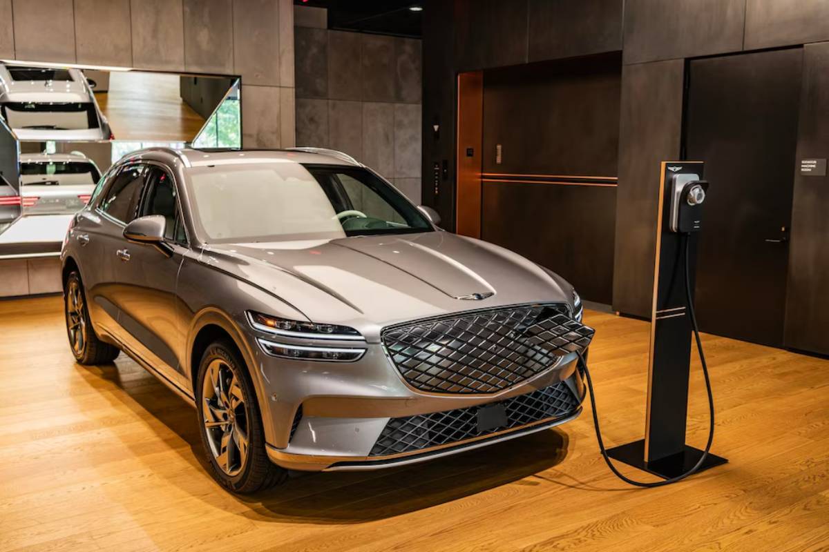 A sleek silver electric SUV is plugged in at a modern charging station inside a stylish showroom with wooden floors and mirrored walls.