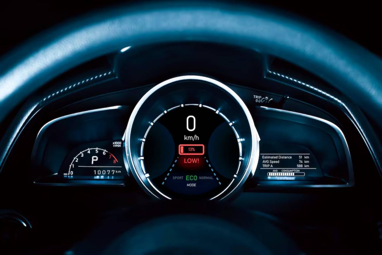 Car dashboard with digital speedometer showing 0 km/h, low battery warning at 13%, and trip details displayed on the right.