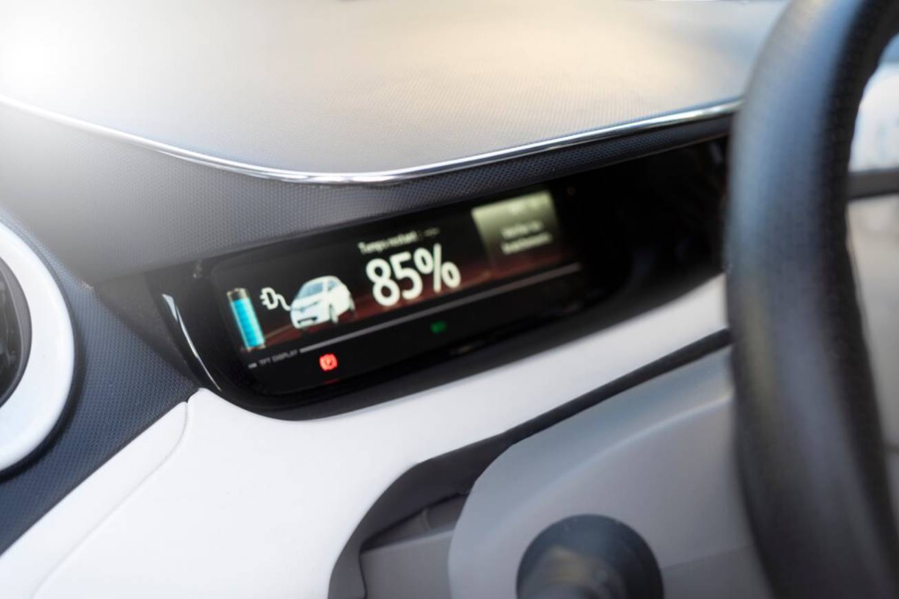 Dashboard display of an electric vehicle showing battery charge at 85% alongside a car icon, with a soft focus on the steering wheel.