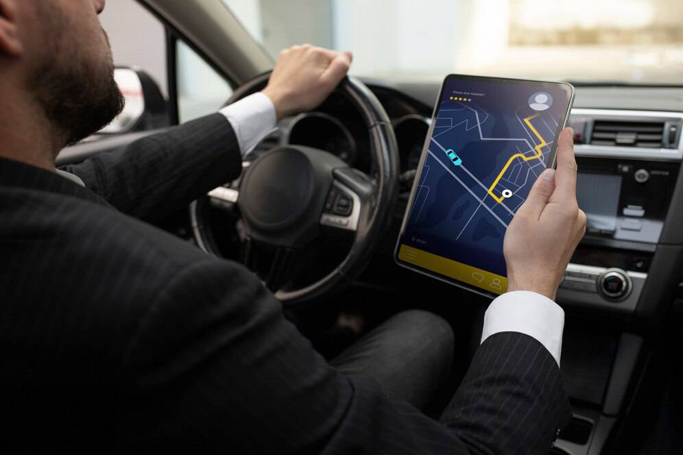 A businessman in a suit drives while using a tablet to navigate a map, showcasing a route with highlighted pathways in a car.