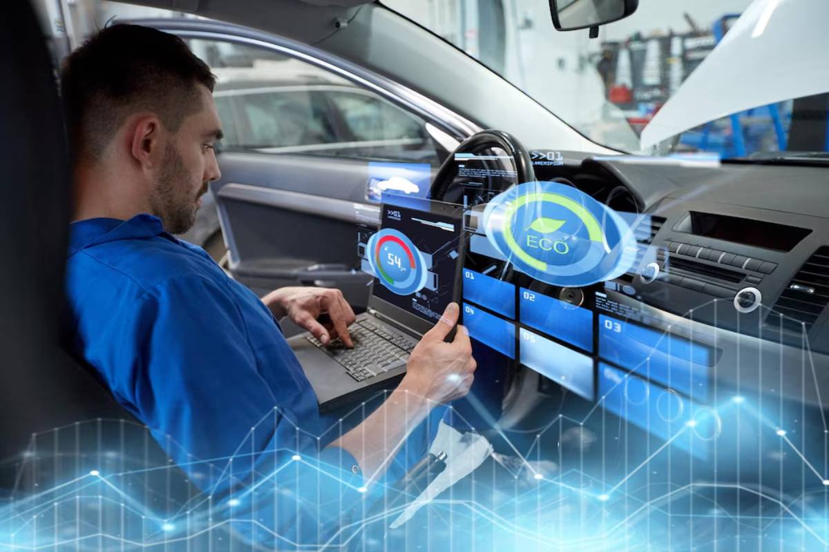 A technician in a blue shirt uses a laptop, surrounded by digital car diagnostics and performance metrics in a modern vehicle interior.