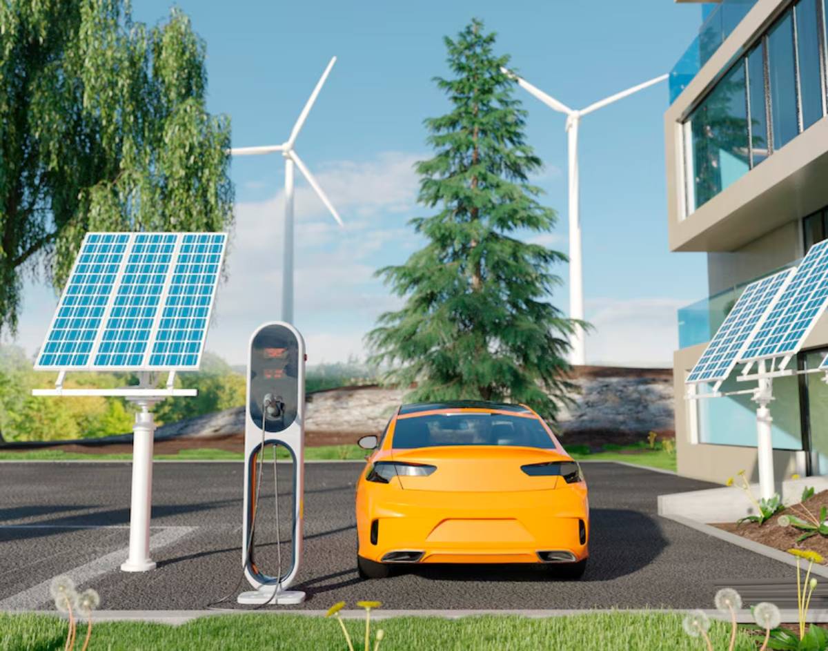 An orange electric car is parked next to a solar panel and charging station, with wind turbines and greenery in the background.