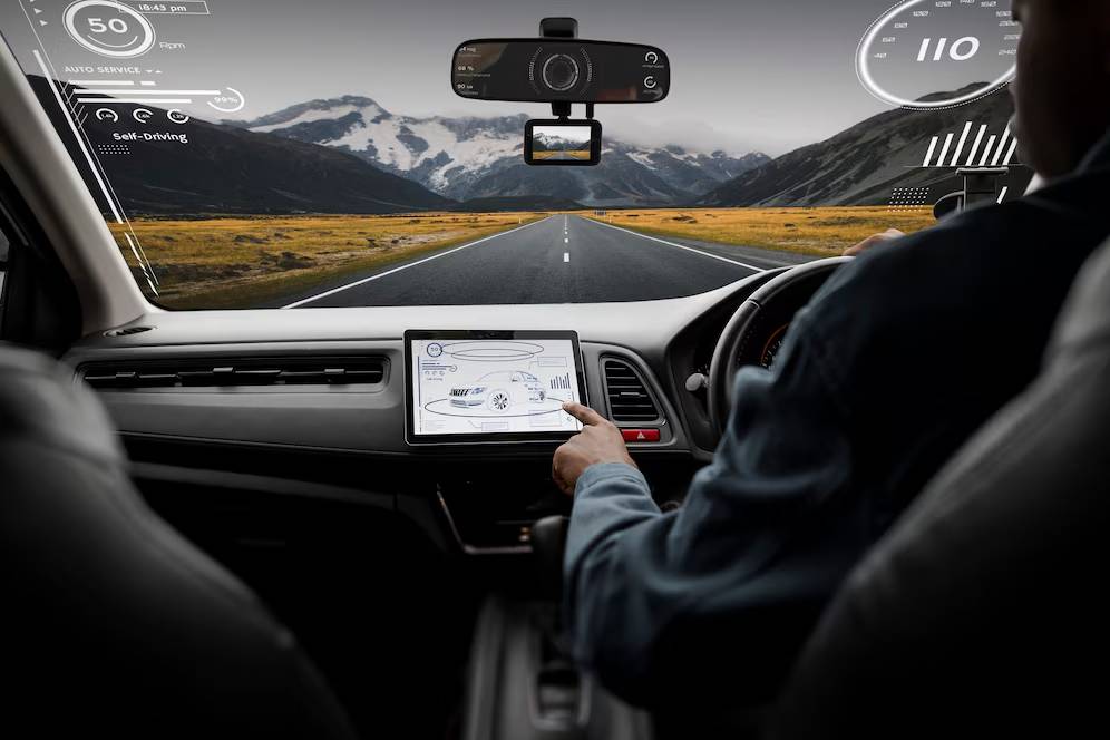 A person in a self-driving car interacts with a digital dashboard displaying speed and service stats against a mountainous road backdrop.