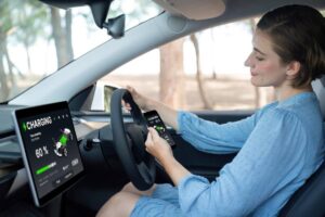 A person in a light blue dress is seated in a car, monitoring a charging screen displaying a 60% battery level.