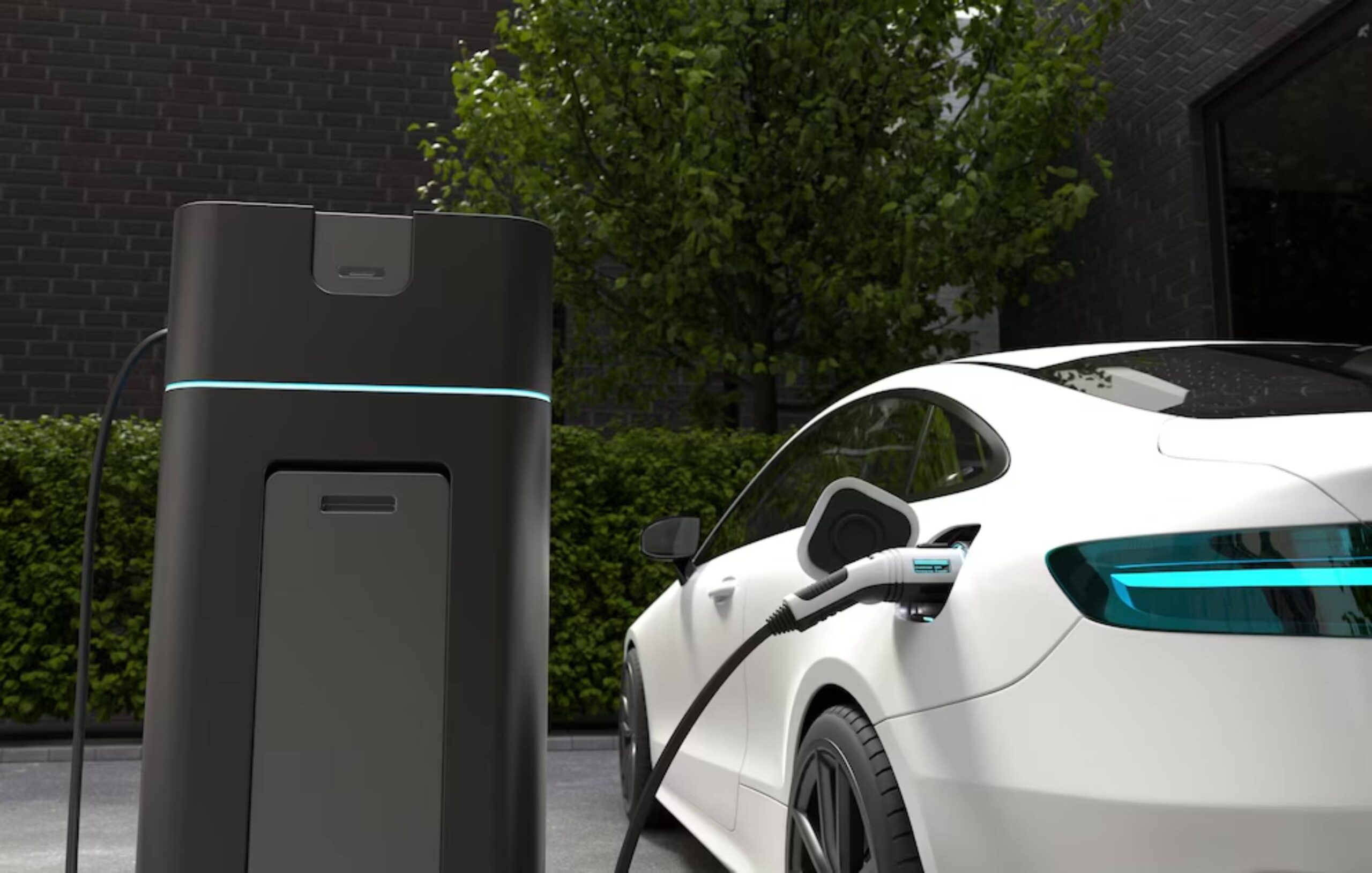 A white electric car is plugged into a sleek black charging station, surrounded by greenery and a modern brick wall backdrop.