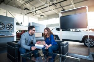 A man and a woman are engaged in a discussion at a modern car dealership, surrounded by vehicles and promotional displays.
