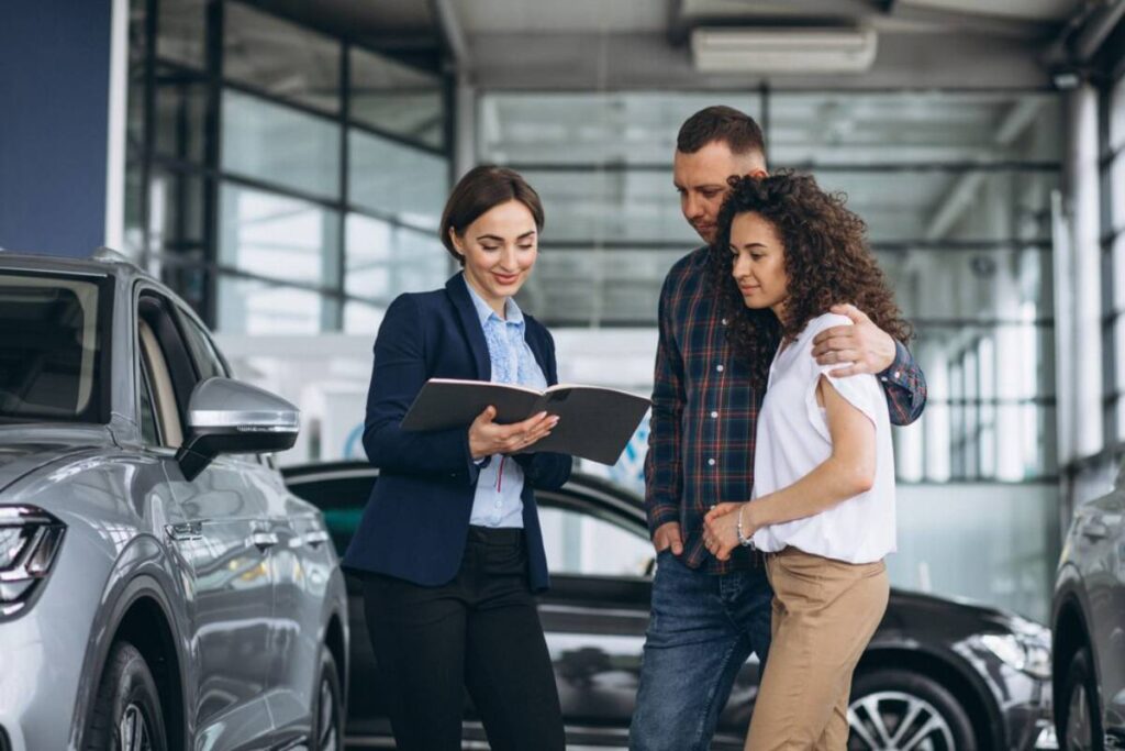 A car salesperson discusses options with a couple in a modern dealership, surrounded by gleaming vehicles.