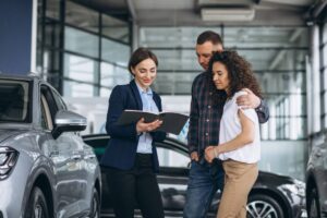 A car salesperson discusses options with a couple in a modern dealership, surrounded by gleaming vehicles.