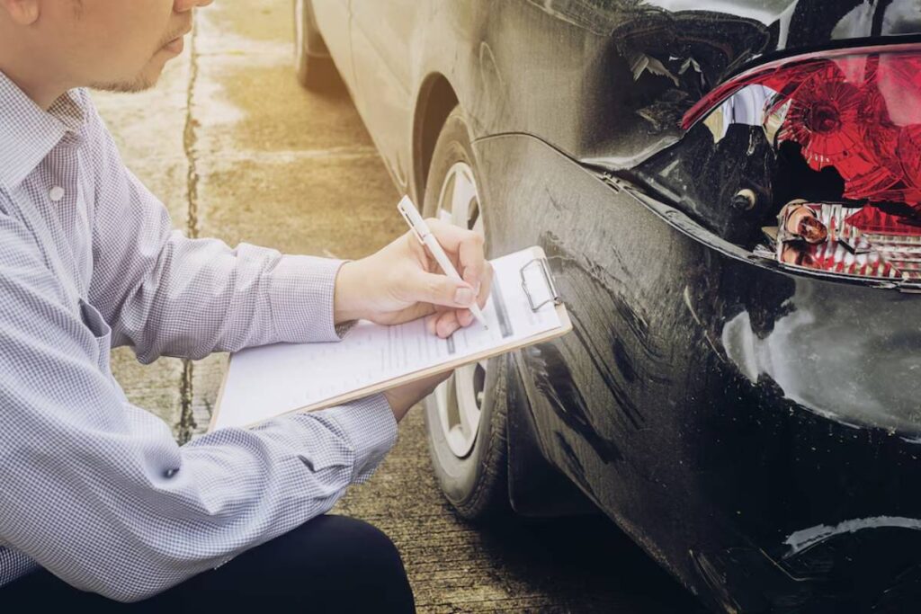 An insurance adjuster inspects a damaged black car, taking notes on a clipboard, assessing the vehicle's rear-end collision.