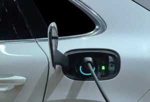 Close-up of a white electric vehicle's charging port with a plugged-in charger, showcasing charging indicators and a glossy finish.
