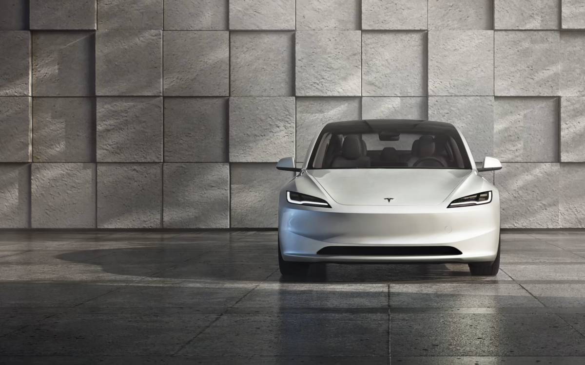 A white electric car charges at a station, with a brightly lit bridge in the background under a night sky.