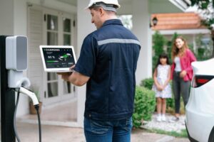 A white electric car is charging outside a modern home, while a family walks towards the entrance, enjoying their time together.