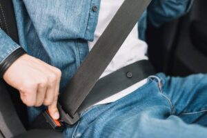 A person fastening their seatbelt in a vehicle, wearing a denim jacket and blue jeans, ensuring safety while driving.